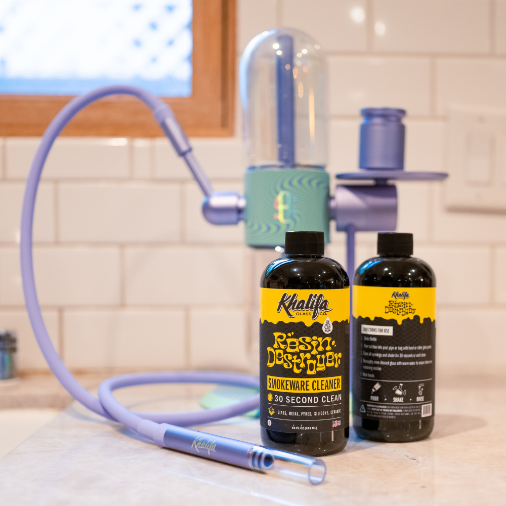 Two bottles of Khalifa Clean Smokeware Cleaner on a kitchen counter with a faucet in the background.